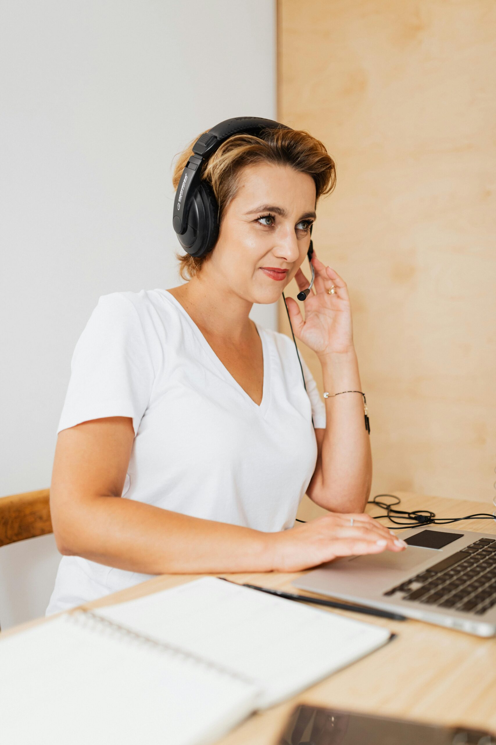 A woman in headphones works at a laptop in a modern office setting.